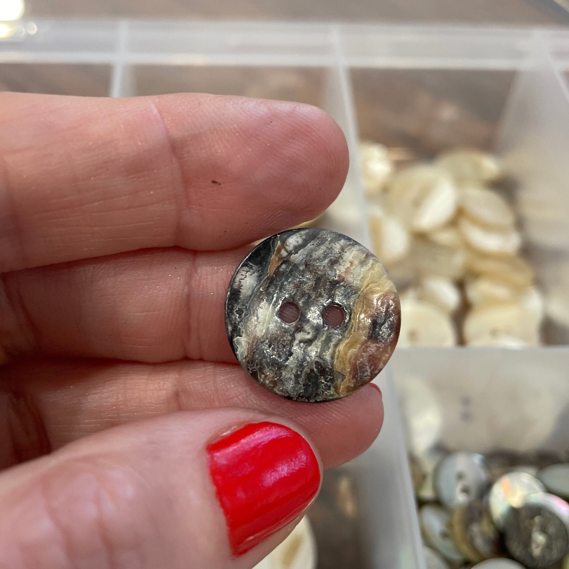Hand holding a button with a blurred background of button collection