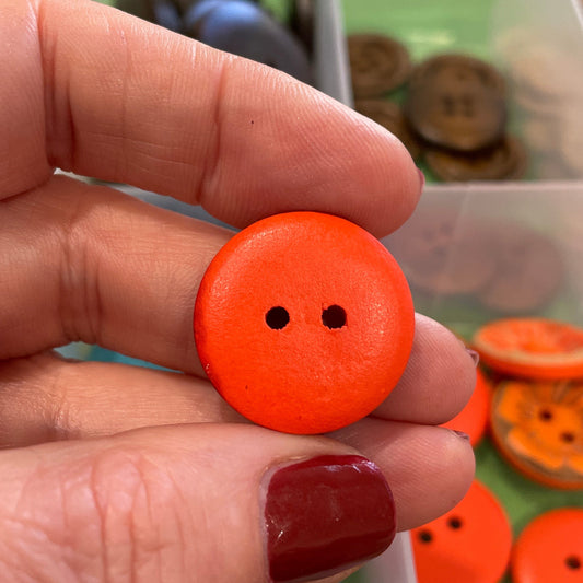 Hand holding an orange button with a background of various colored buttons in a container.