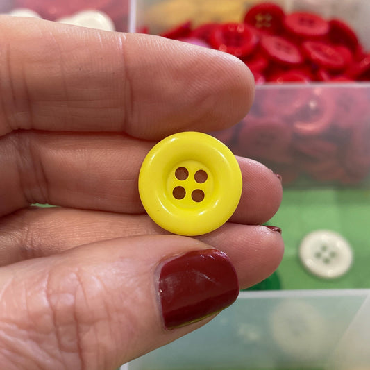 Hand holding a yellow button with a background of colorful buttons in a box