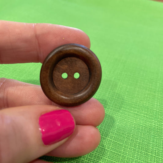 Wooden button held between fingers against a green background