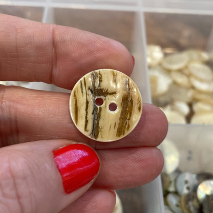Gold button held by a hand with red nail polish, against a background of assorted buttons.