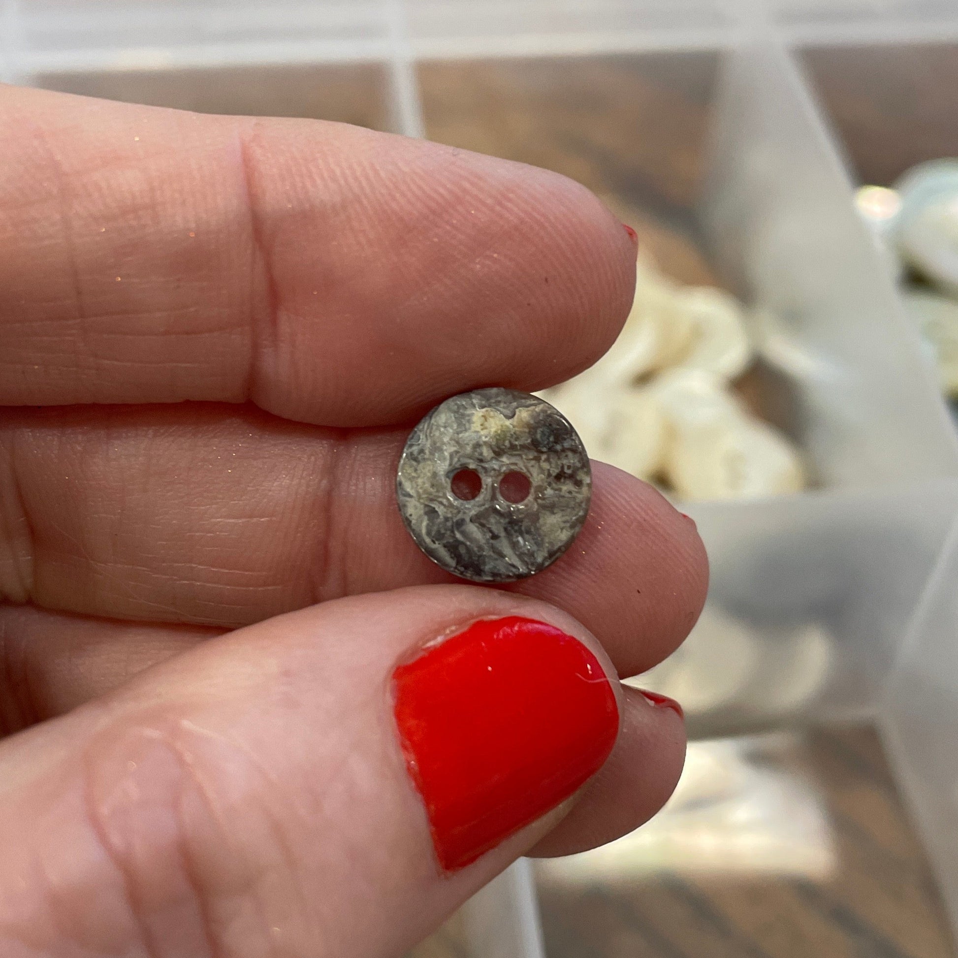 Hand holding two small stones with a clear container of more stones in the background