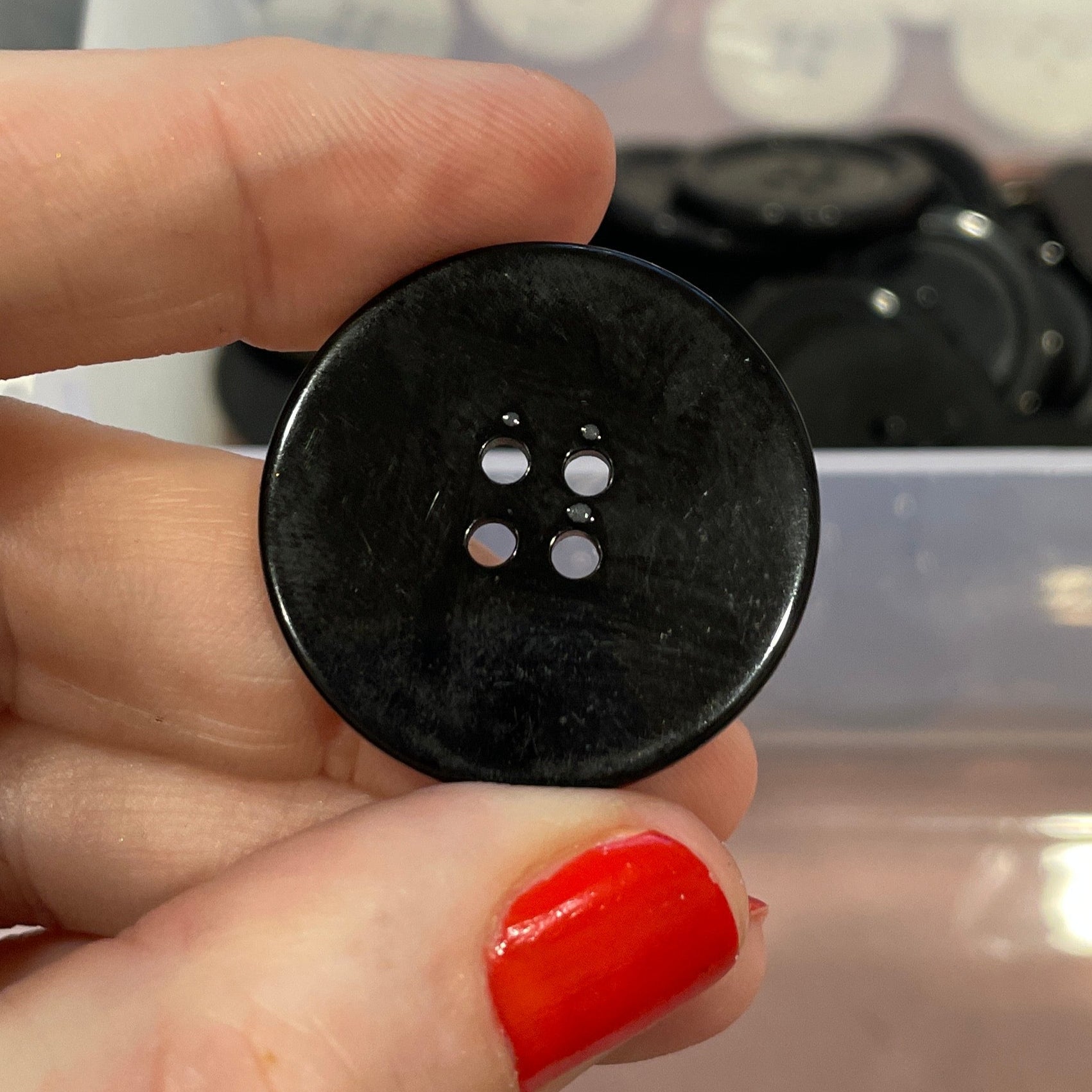 Hand holding a black button with a clear container of buttons in the background