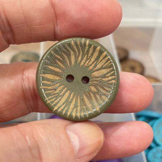 Hand holding a decorative button with a sunburst pattern against a background of colorful buttons.
