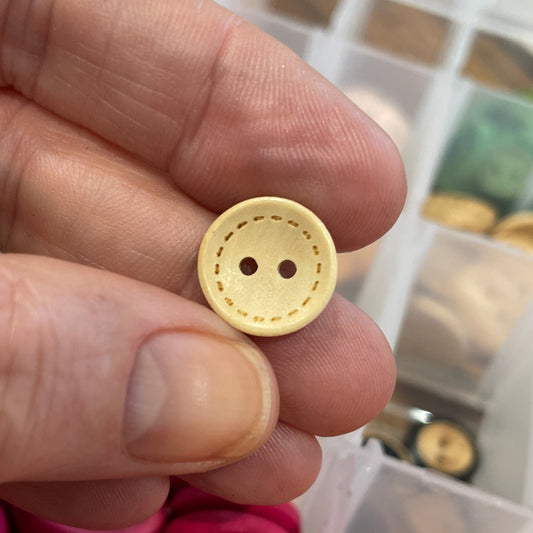 Hand holding a yellow button with a container of colorful buttons in the background