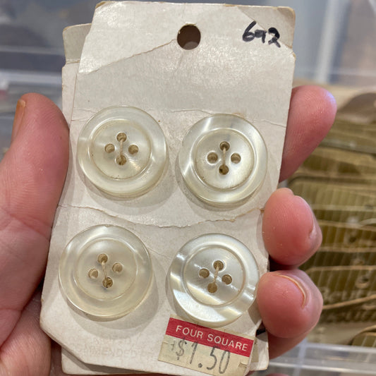 Four white buttons on a card held by a hand with a blurred background