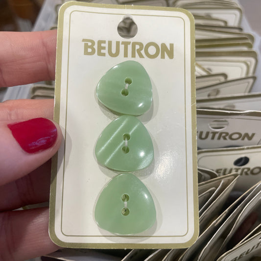 Three green buttons on a Beutron card held by a hand with red nail polish.
