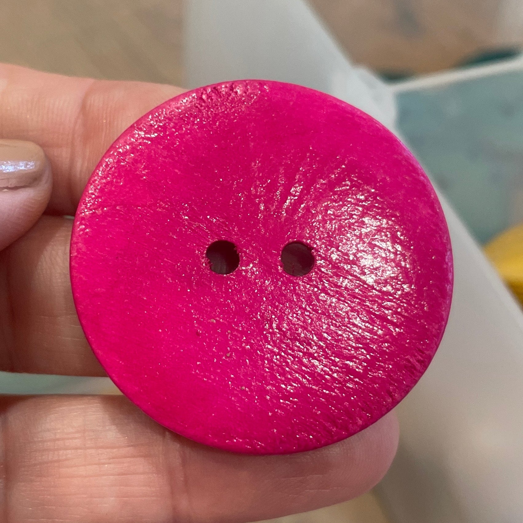 Hand holding a pink button with a blurred background of colorful objects