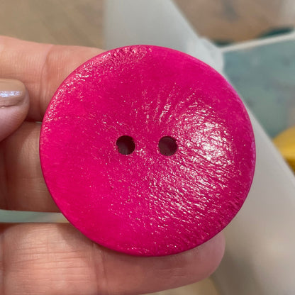 Hand holding a pink button with a blurred background of colorful objects