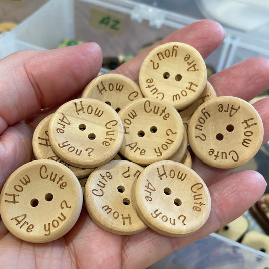 Hand holding wooden buttons with engraved text, blurred background of more buttons.