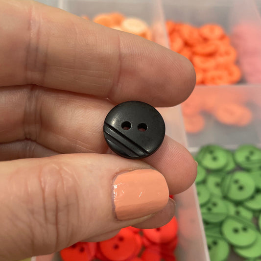 Hand holding a black button with a container of colorful buttons in the background