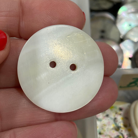 White button held by a hand with red nail polish, blurred background of button display