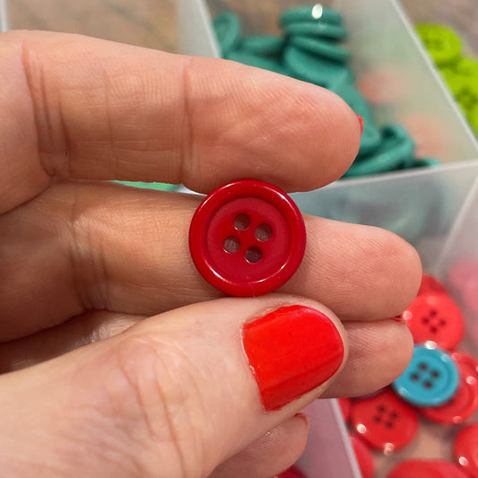 Hand holding a red button with a container of buttons in the background