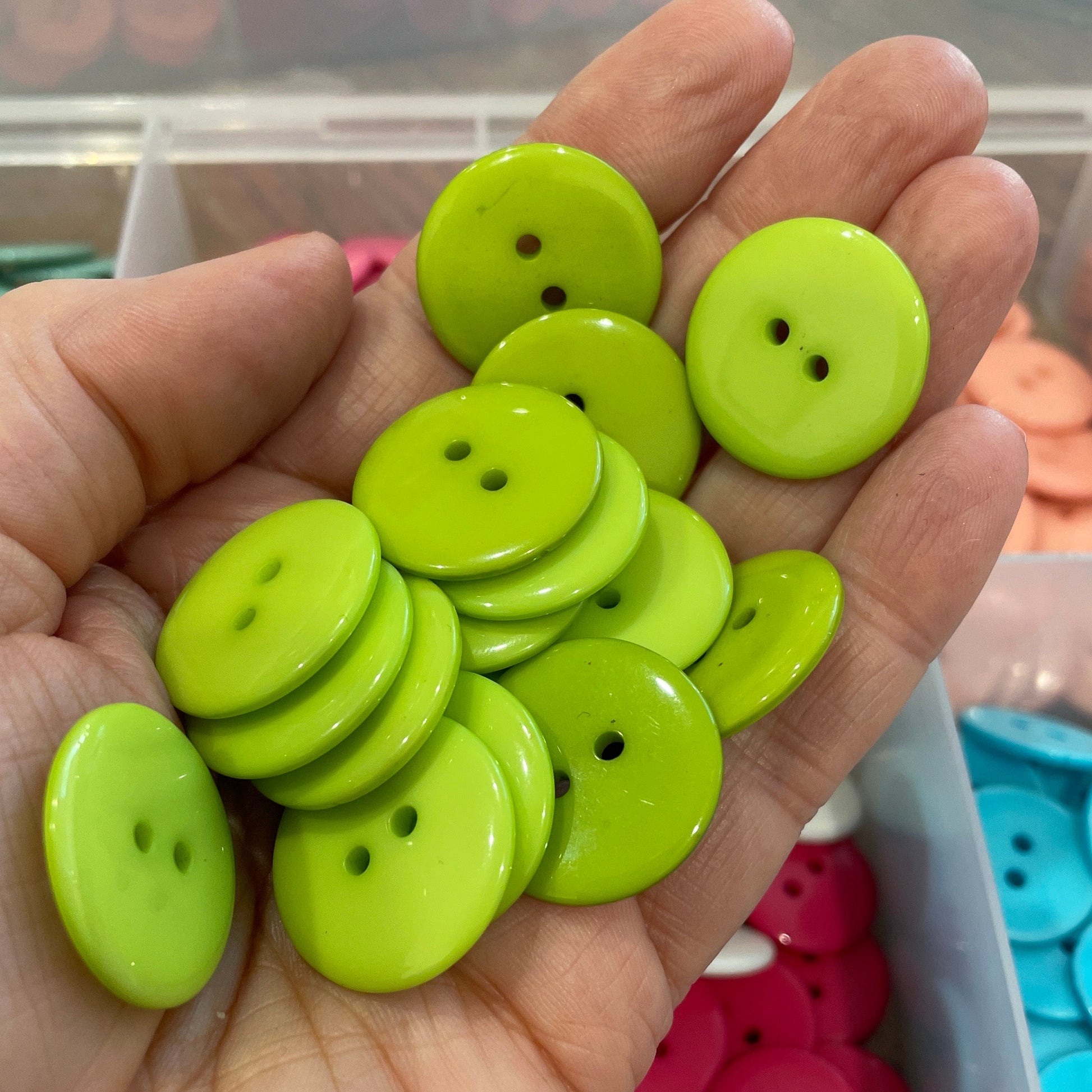 Hand holding green buttons with a container of colorful buttons in the background