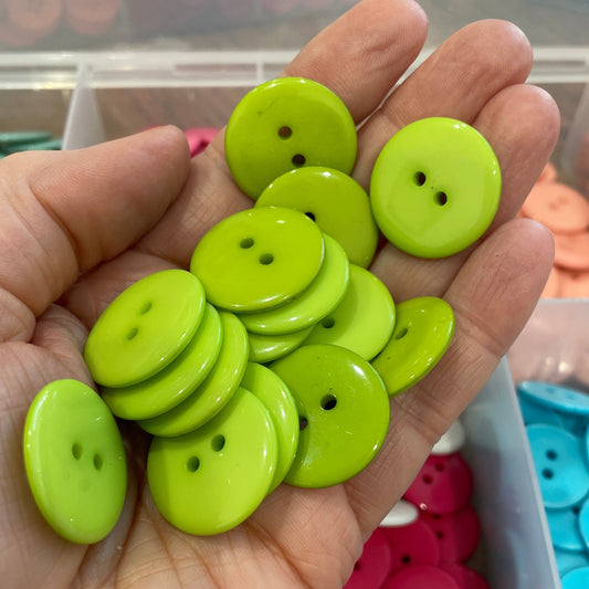 Hand holding green buttons with a container of colorful buttons in the background