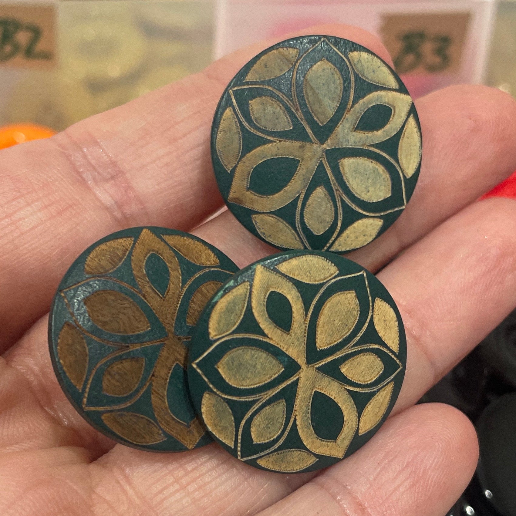 Hand holding decorative buttons with a button collection container in the background