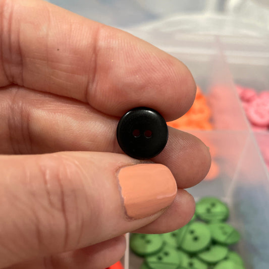 Hand holding a black button with a container of green and red buttons in the background