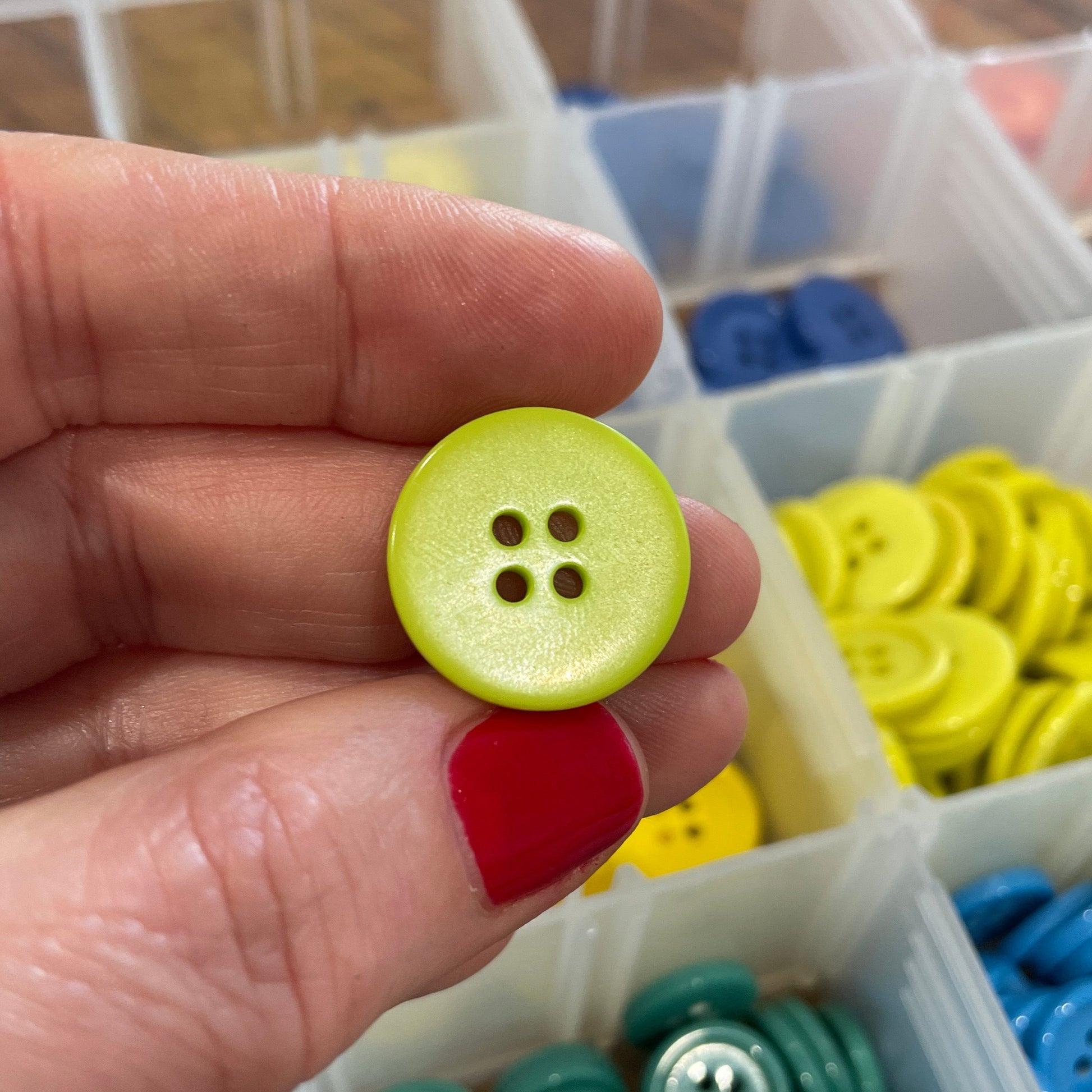 Hand holding a yellow button with a container of colorful buttons in the background