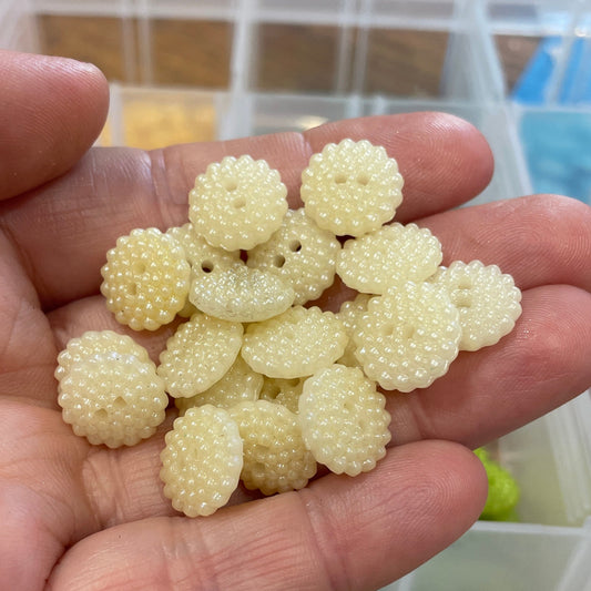 Hand holding a cluster of white button-like objects with a button organizer in the background.