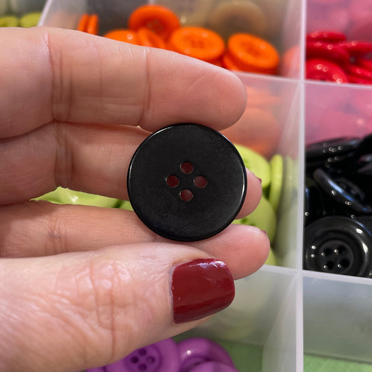 Hand holding a black button with a container of colorful buttons in the background