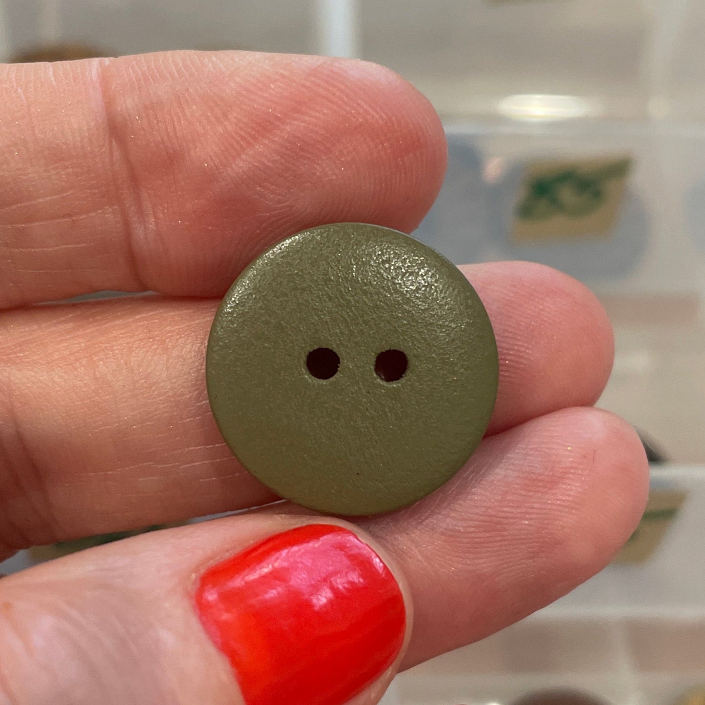 Hand holding a green button with a clear container of buttons in the background