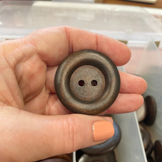 Hand holding a ceramic button with a blurred container of buttons in the background