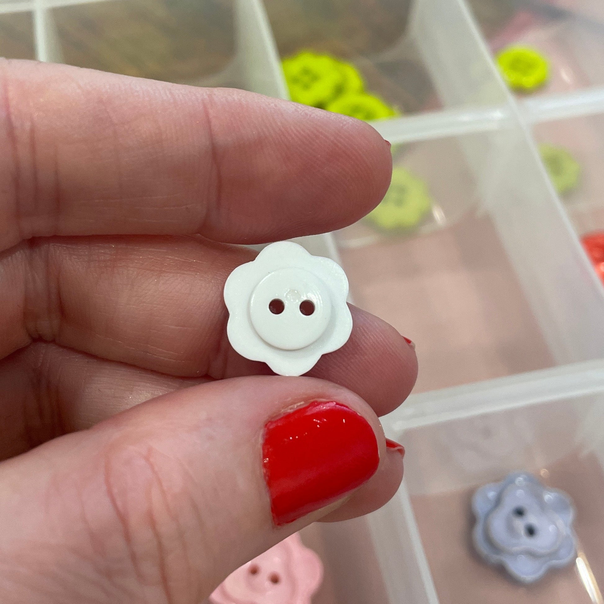 Hand holding a white flower-shaped button with a clear container of buttons in the background