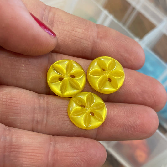 Yellow buttons held between fingers with a container of colorful buttons in the background.