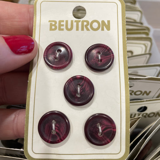 Beutron buttons held by a hand with red nail polish.