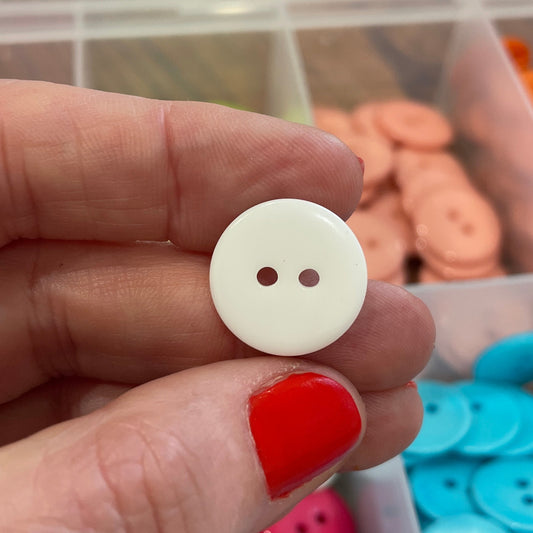 Hand holding a white button with two holes, with colorful buttons in the background