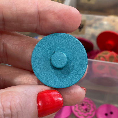Hand holding a blue button with a background of various buttons in containers