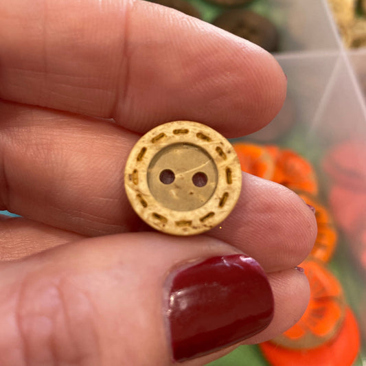 Gold decorative button held by a hand with a colorful assortment of buttons in the background.