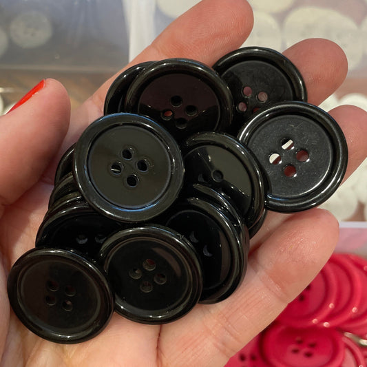 Hand holding a collection of black buttons with a background of various colored buttons.