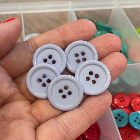 Hand holding white buttons with a container of colorful buttons in the background