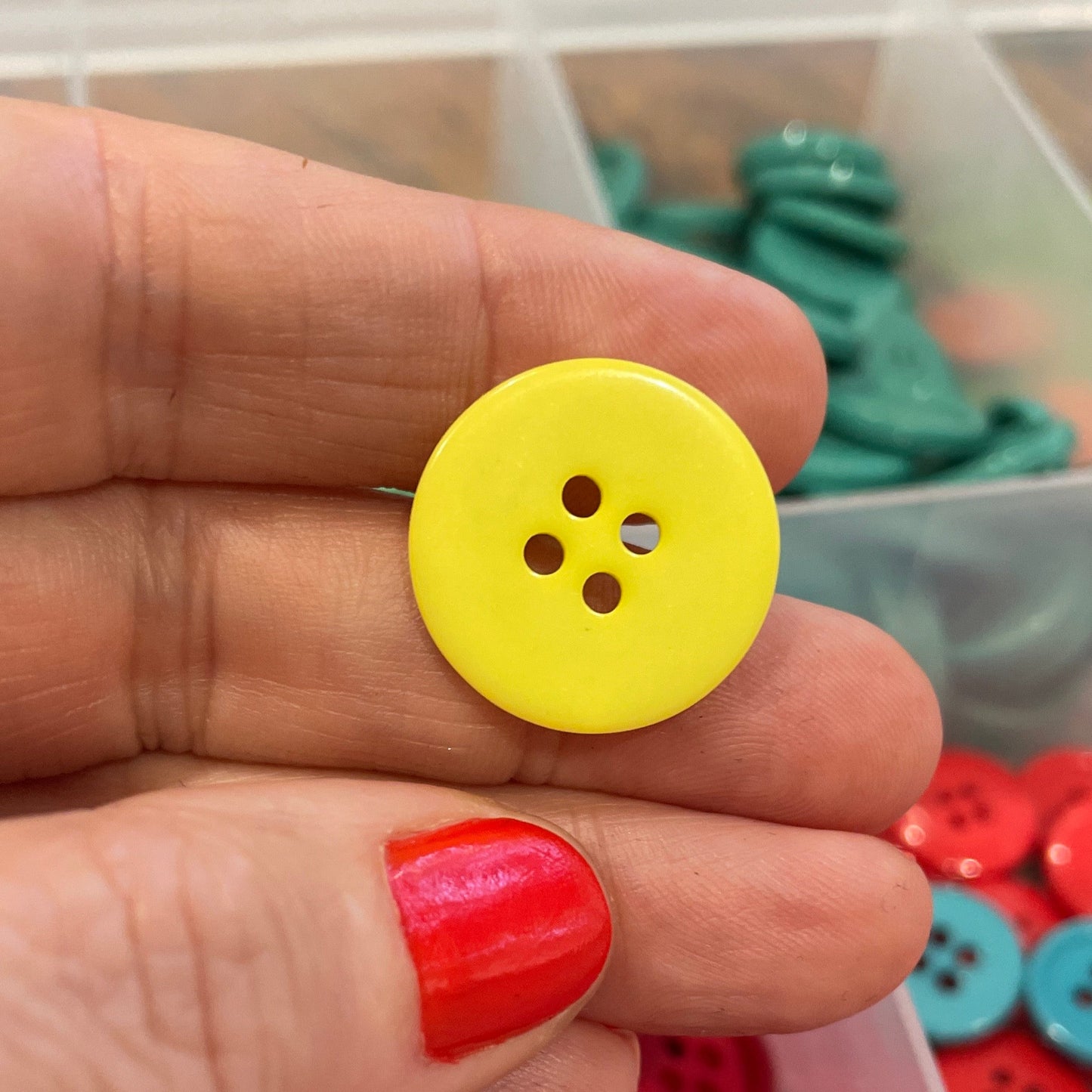 Hand holding a yellow button with a container of red buttons in the background