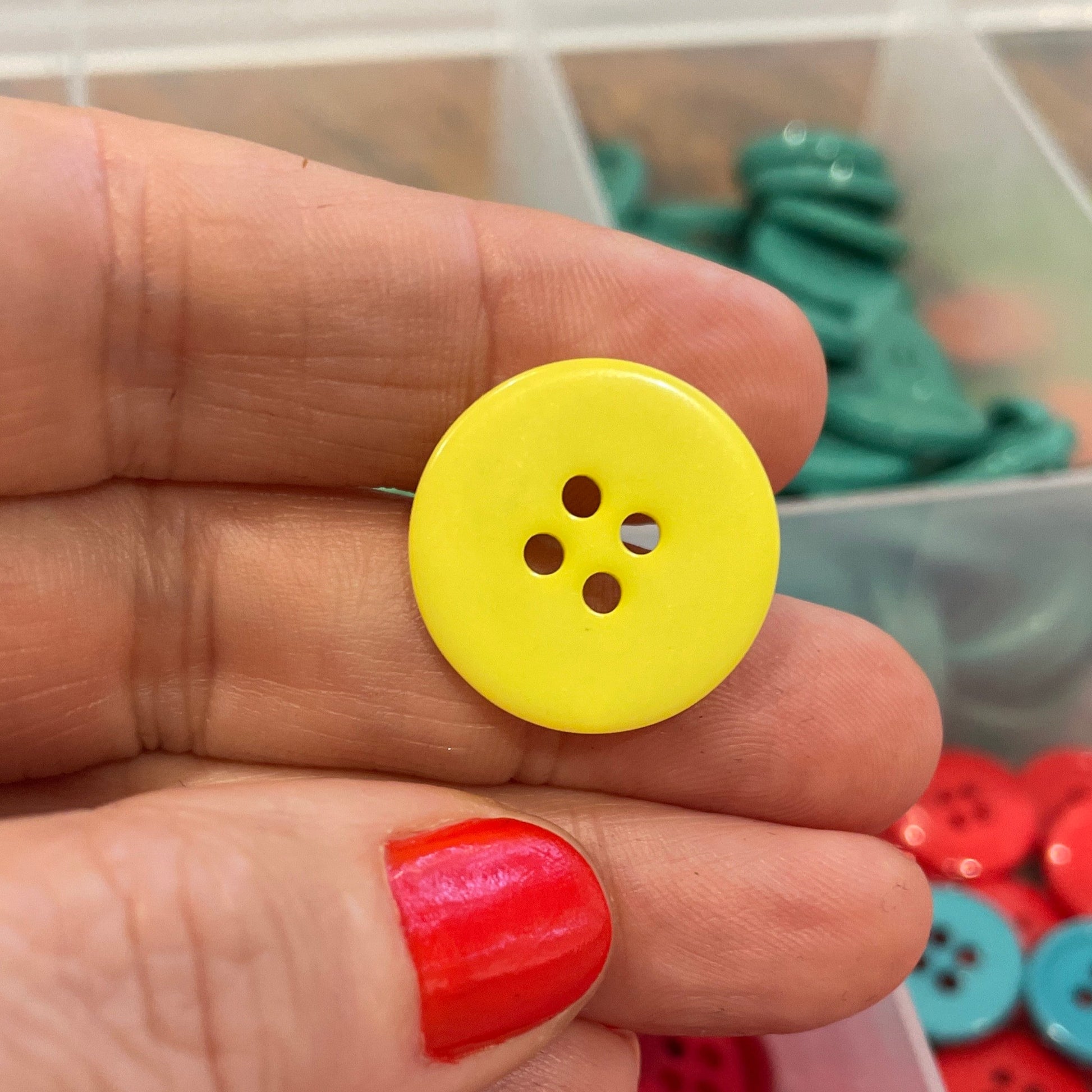 Hand holding a yellow button with a container of red buttons in the background