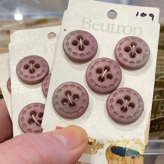 Hand holding a card with six brown buttons on a blurred background