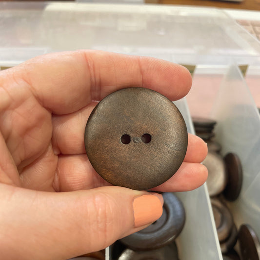 Hand holding a brown button with two holes above a container of buttons.