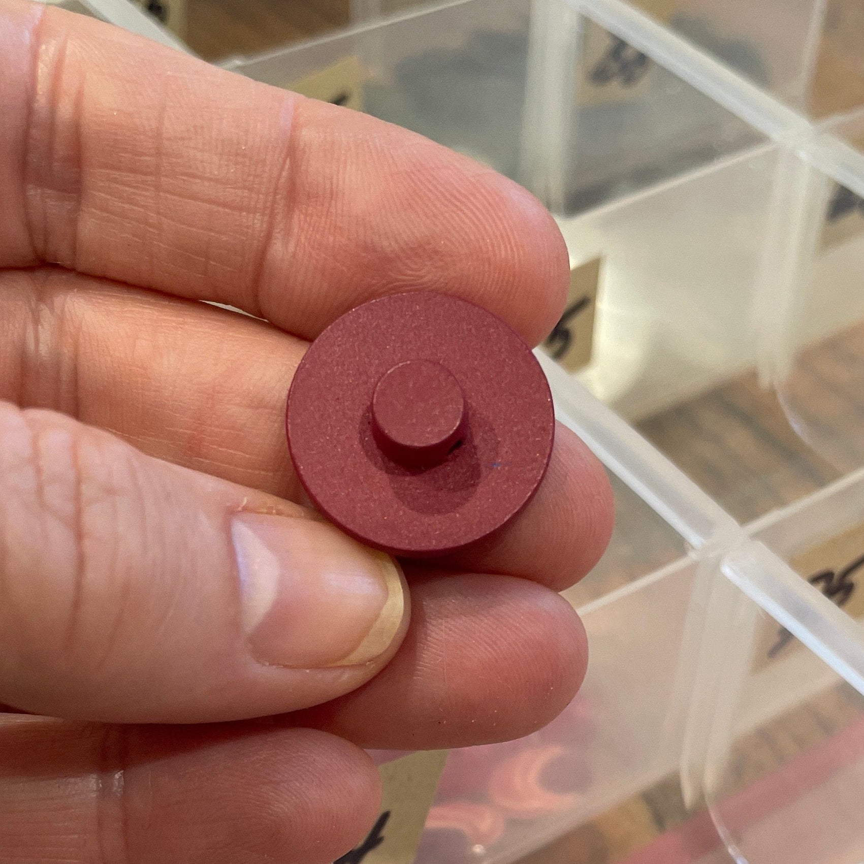 Hand holding a small red circular button with a clear container in the background