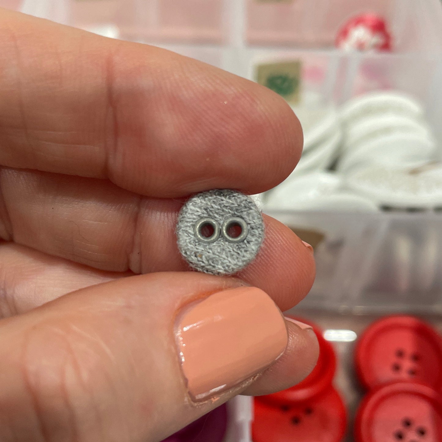 Hand holding a decorative button with a blurred background of button collection