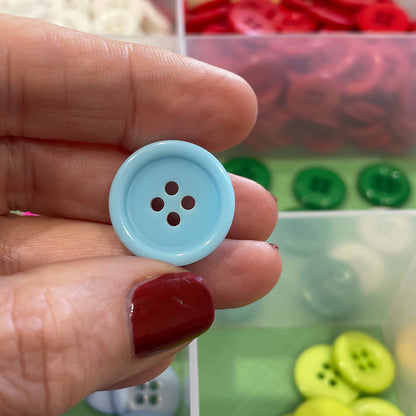 Hand holding a light blue button with a clear container of buttons in the background