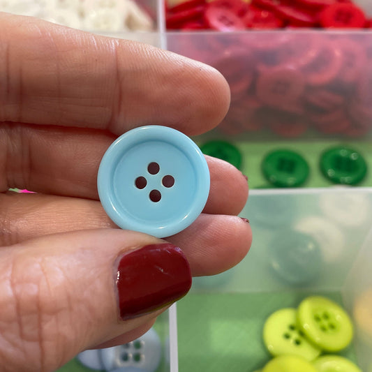 Hand holding a light blue button with a clear container of buttons in the background