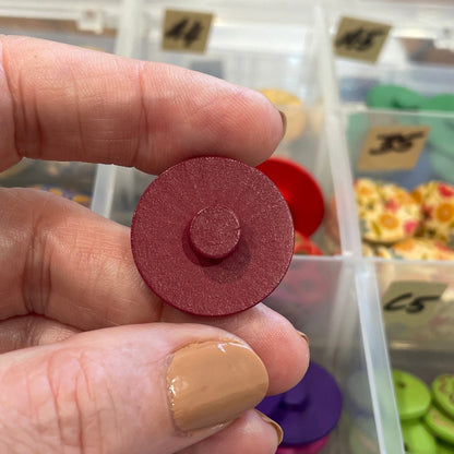 Hand holding a red button in front of a container filled with various buttons.