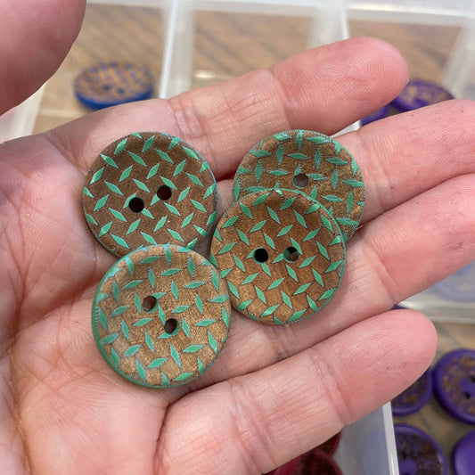 Three green textured buttons held in a hand with a container of buttons in the background.