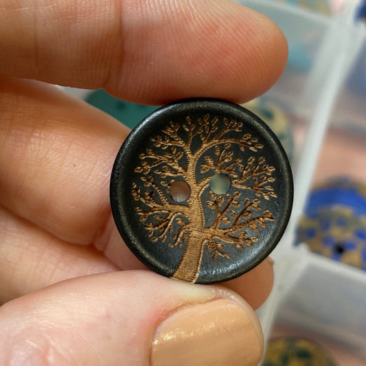 Hand holding a decorative button with intricate design, against a blurred background of a jewelry box.