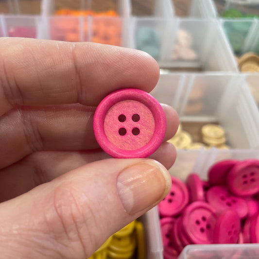 Hand holding a pink button with a container of buttons in the background