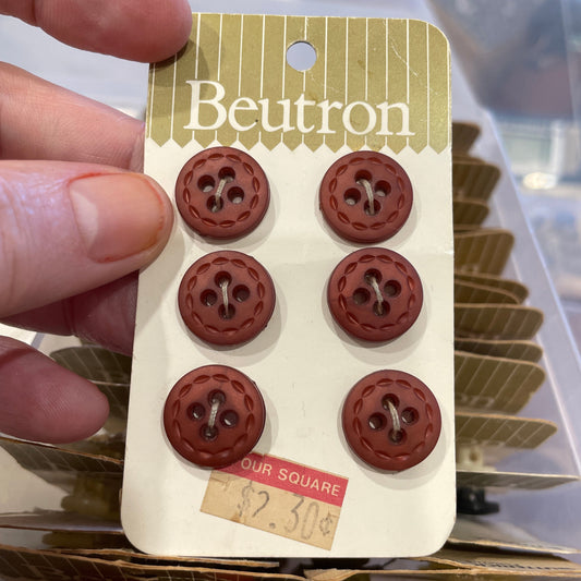 Card with six brown buttons held by a hand, with a blurred background