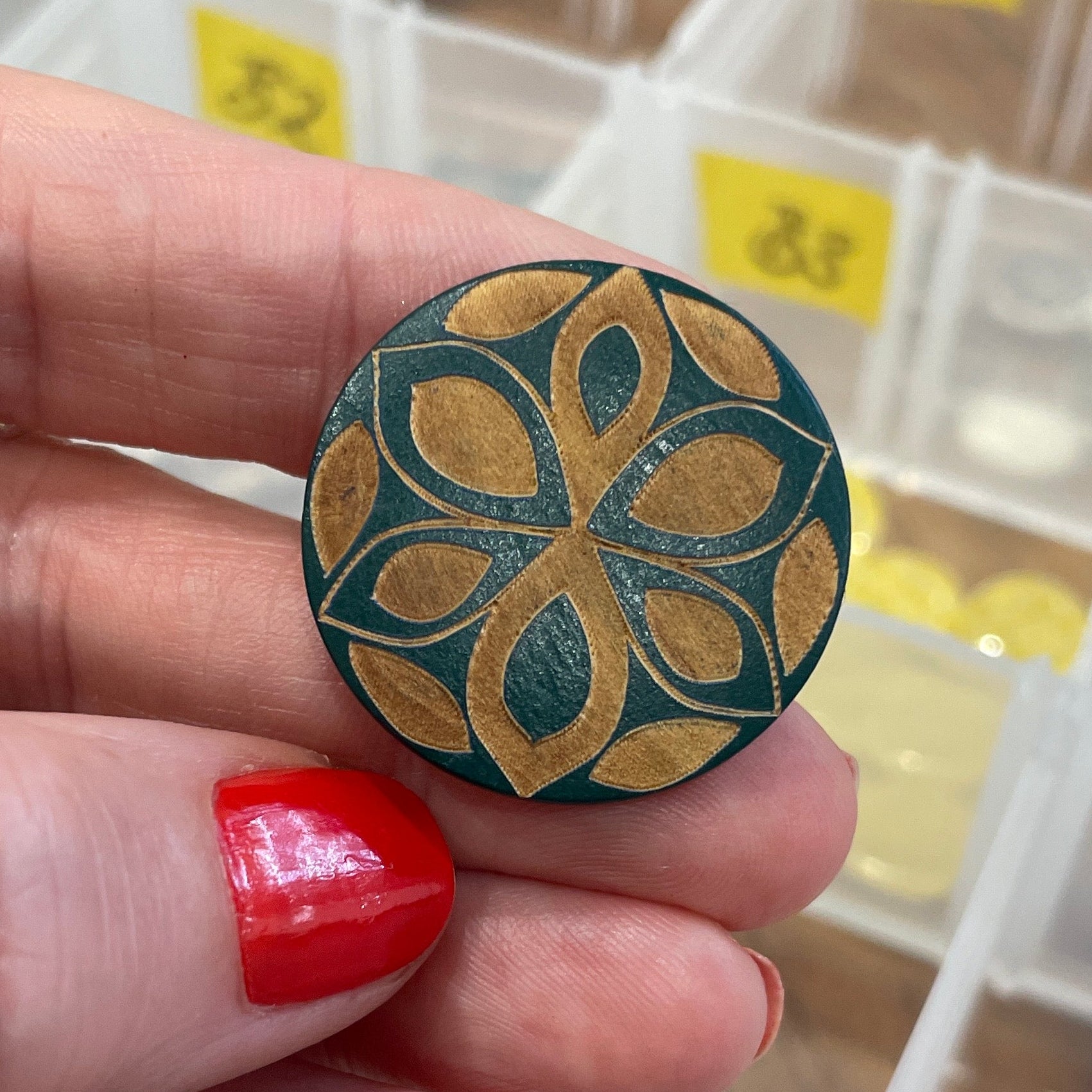 Hand holding a decorative button with a floral design, against a background of a button organizer.