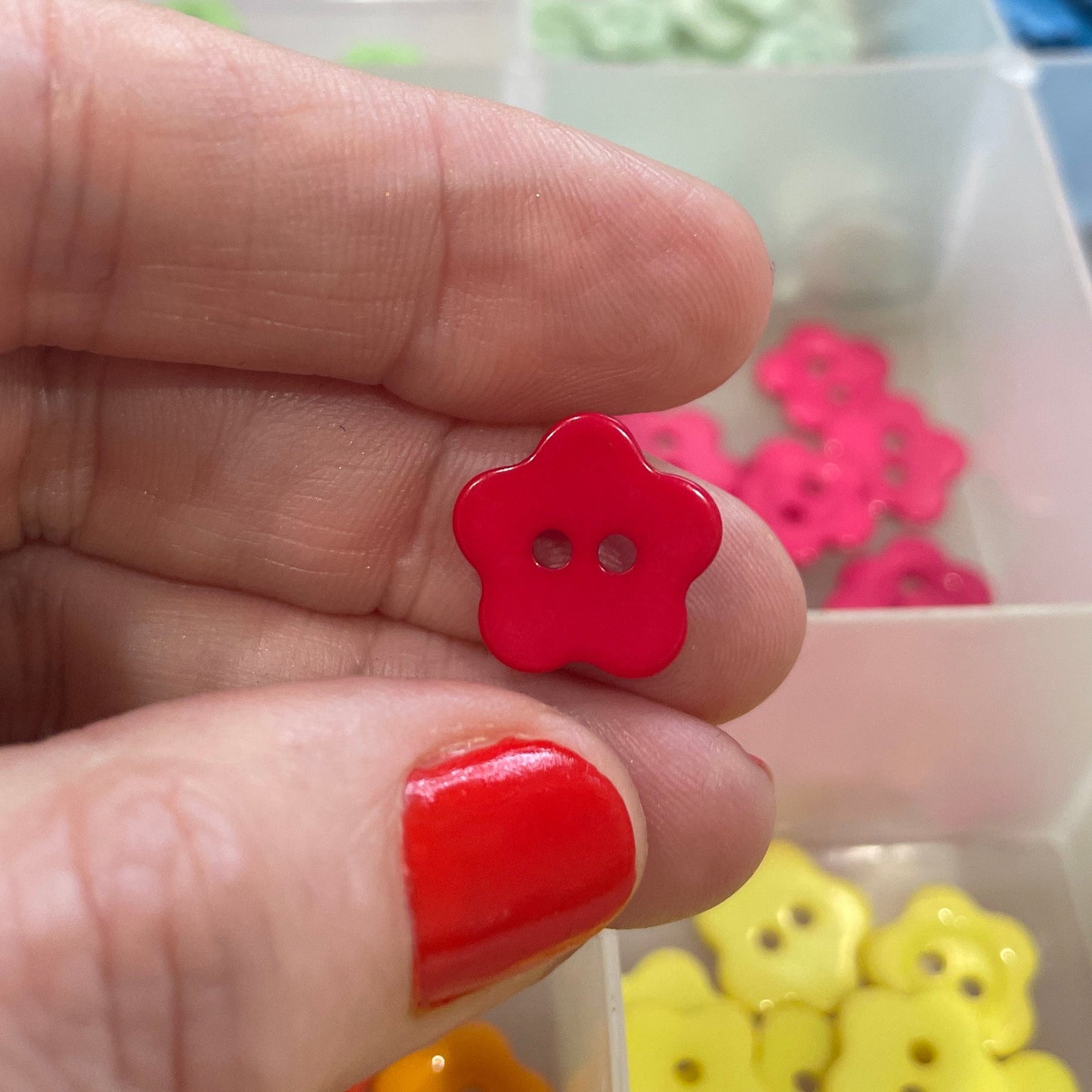 Red button held between fingers with a container of colorful buttons in the background
