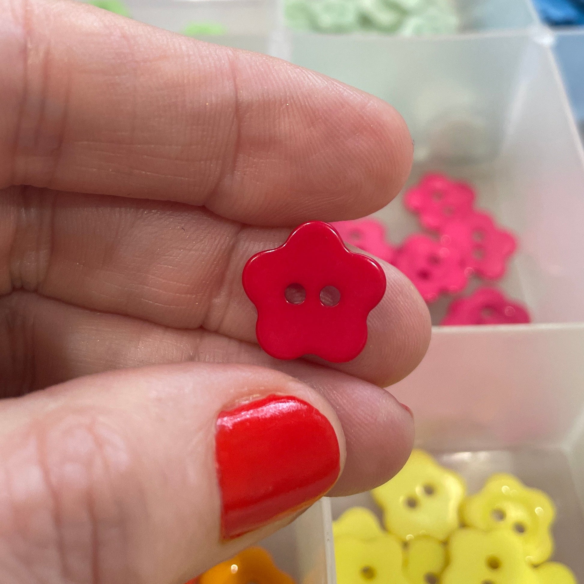 Red button held between fingers with a container of colorful buttons in the background